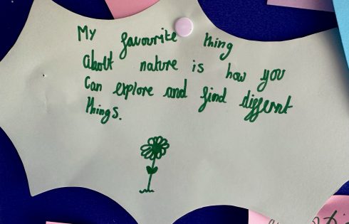 A green piece of paper is pinned to a blue pinboard and it says "My favourite thing about nature is how you can explore and find different things"